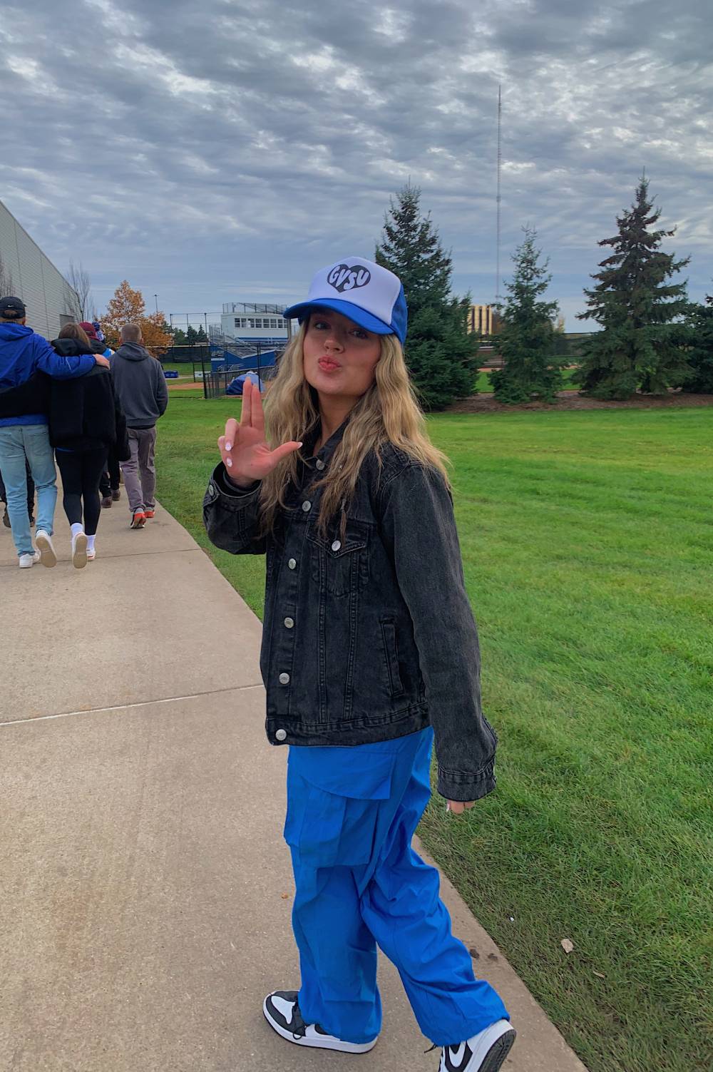 Image 1 of 2 Female student holding fingers in a L-shape with a hat on, turning around